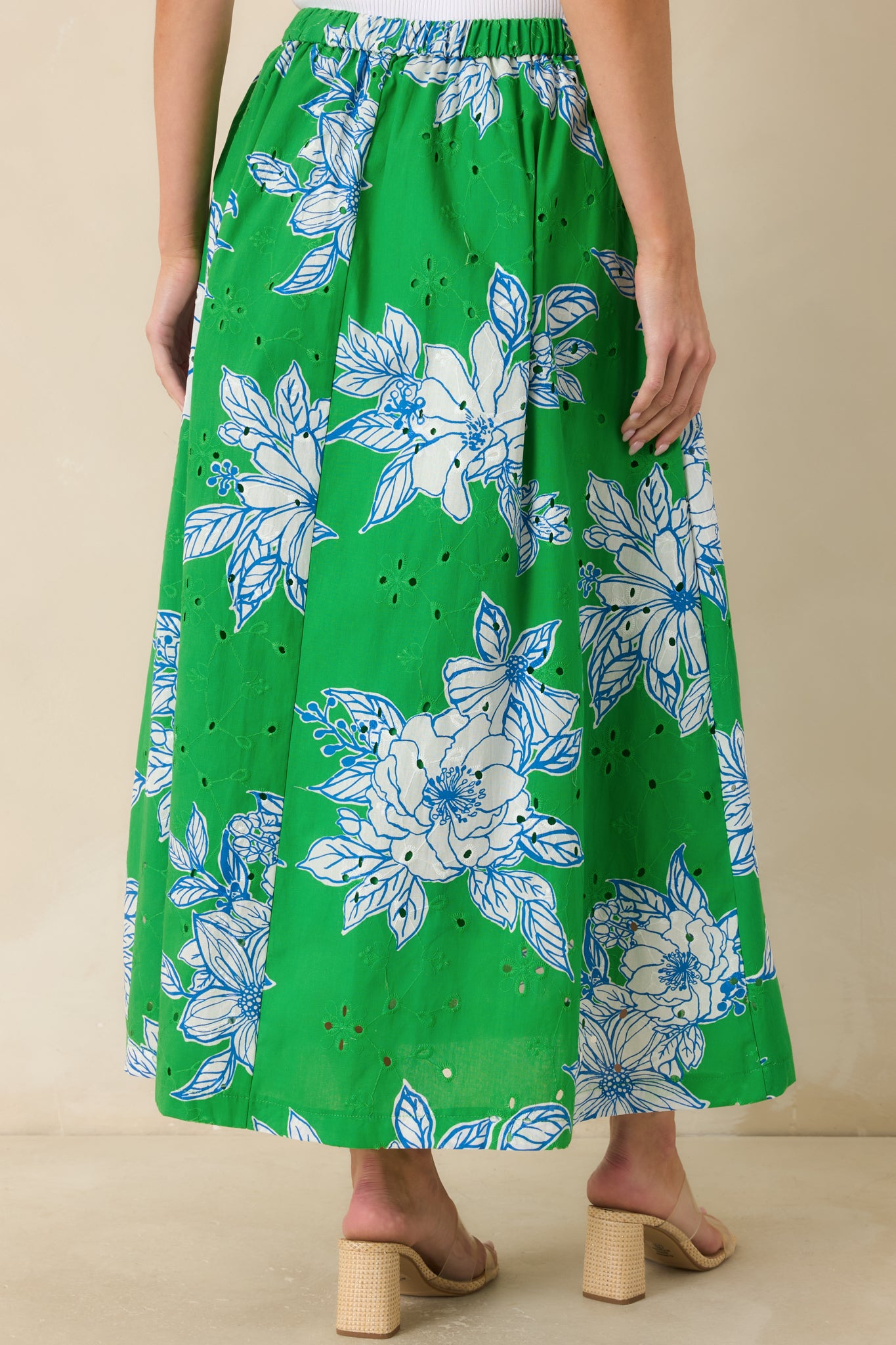 Back view of the green and white floral midi skirt featuring an elastic waistband, side pockets, and flowing eyelet fabric silhouette.

