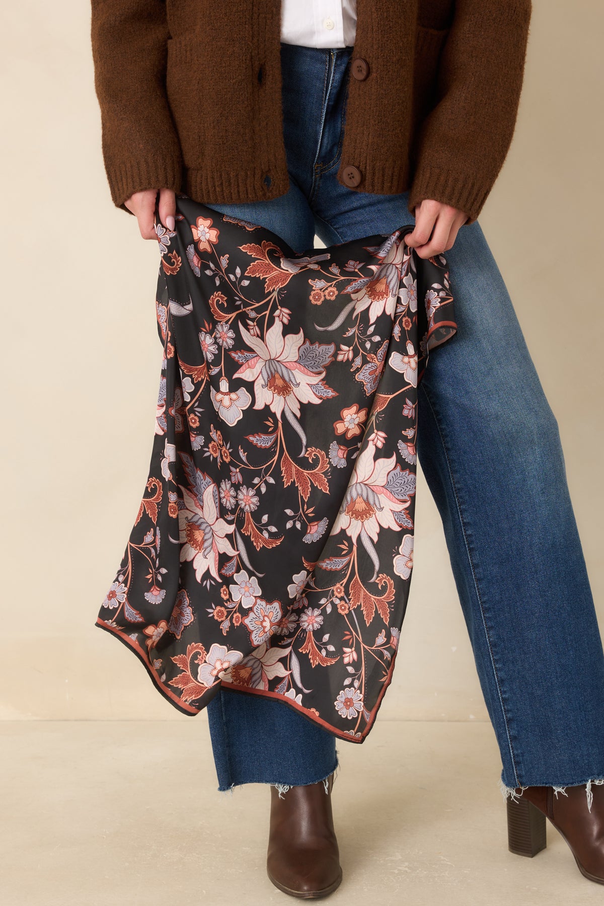 A rust border outlines the botanical hair scarf, complementing its detailed flowers and multicolored leaves against black.