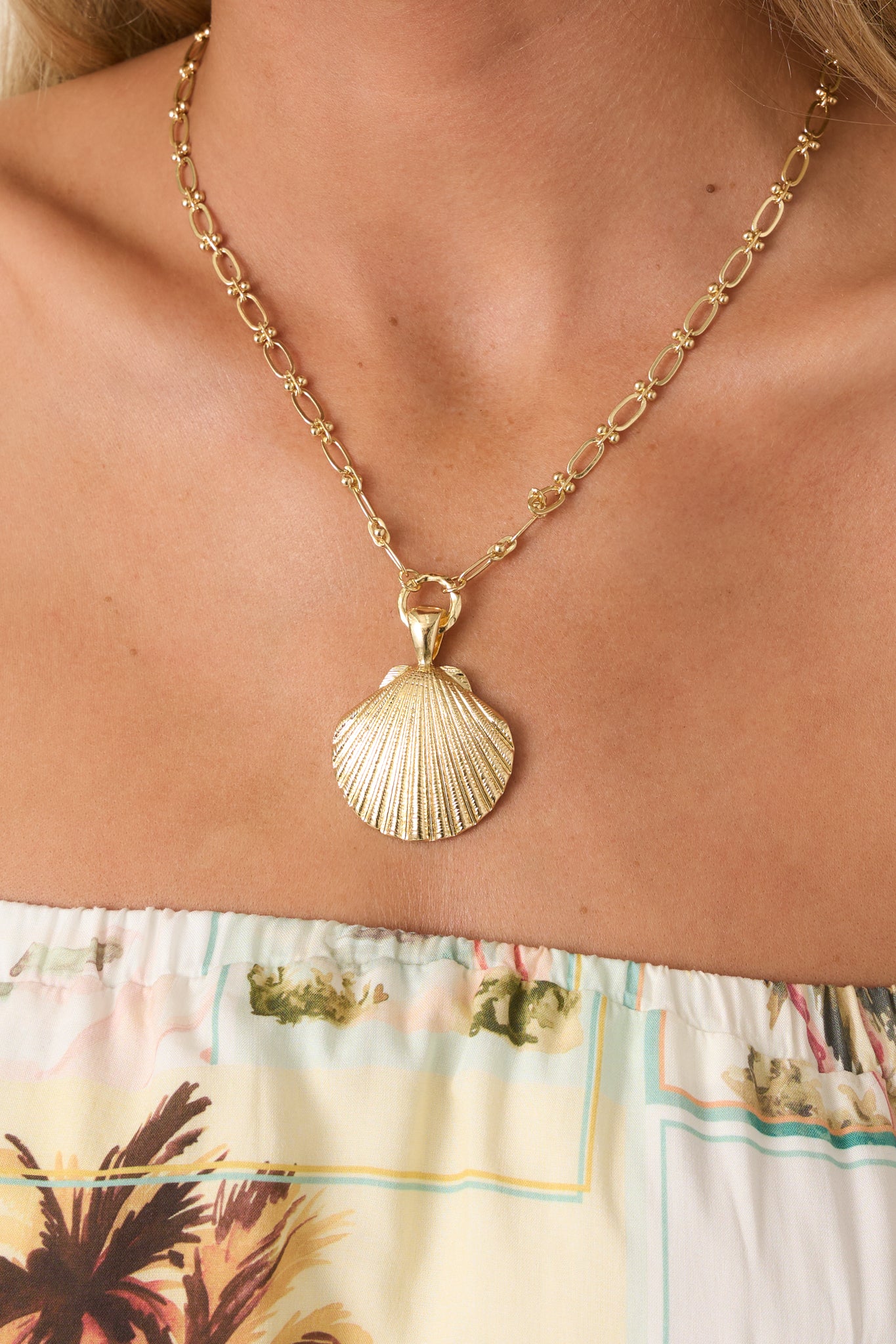 Close-up detail of necklace showing scallop shell pendant, elongated gold-tone links, and smooth finish.