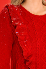 Close up view of this sweater that features a scoop neckline, ruffles around the bust, and a cable knit detail on the front.