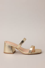 Side view of these gold block heels that feature a square toe, two gold straps across the top of foot, and a block heel.