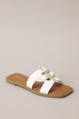Angled front view of these white sandals with square toe, slip-on design, strap with cutouts and gold accent piece over foot.