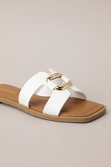 Close up front view of these white sandals with square toe, slip-on design, strap with cutouts and gold accent piece over foot.