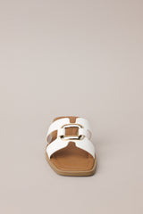 Front view of these white sandals with square toe, slip-on design, strap with cutouts and gold accent piece over foot.
