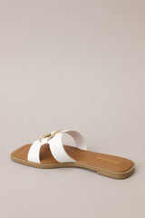 Angled back view of these white sandals with square toe, slip-on design, strap with cutouts and gold accent piece over foot.