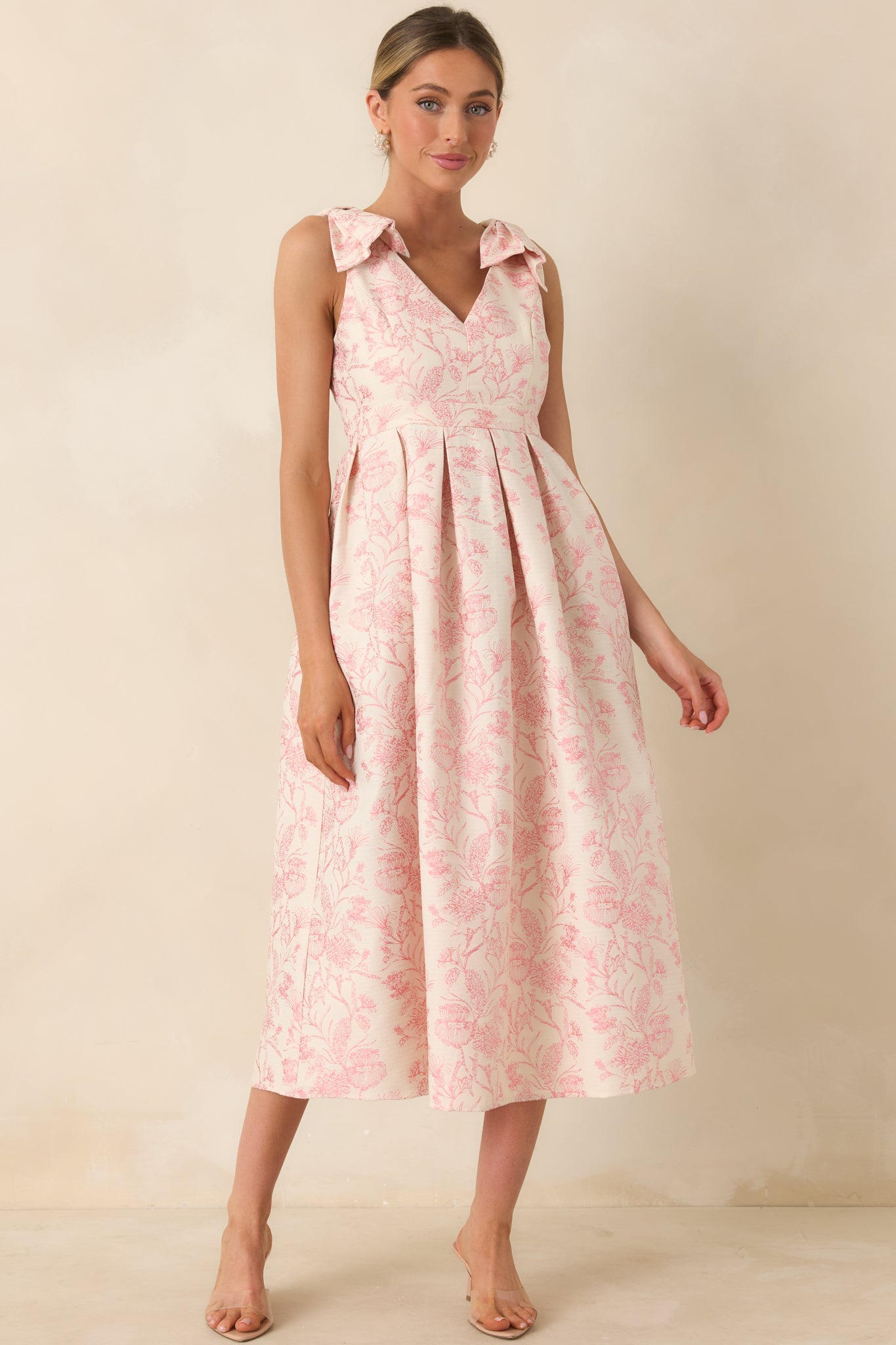 Pink floral midi dress with statement bow straps and a full pleated silhouette, shown from the front.