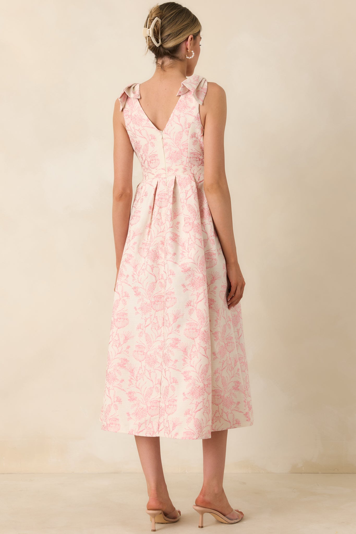 Back view of a pink floral midi dress with bow straps and full pleated skirt, highlighting structured silhouette.