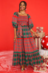 Front view of  this dress that features a square neckline, puff sleeves with elastic cuffs, a fully smocked bust, a self-tie belt at the waist, and a long, exaggerated skirt with alternating plaid patterns. 