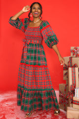 Angled front view of  this dress that features a square neckline, puff sleeves with elastic cuffs, a fully smocked bust, a self-tie belt at the waist, and a long, exaggerated skirt with alternating plaid patterns. 