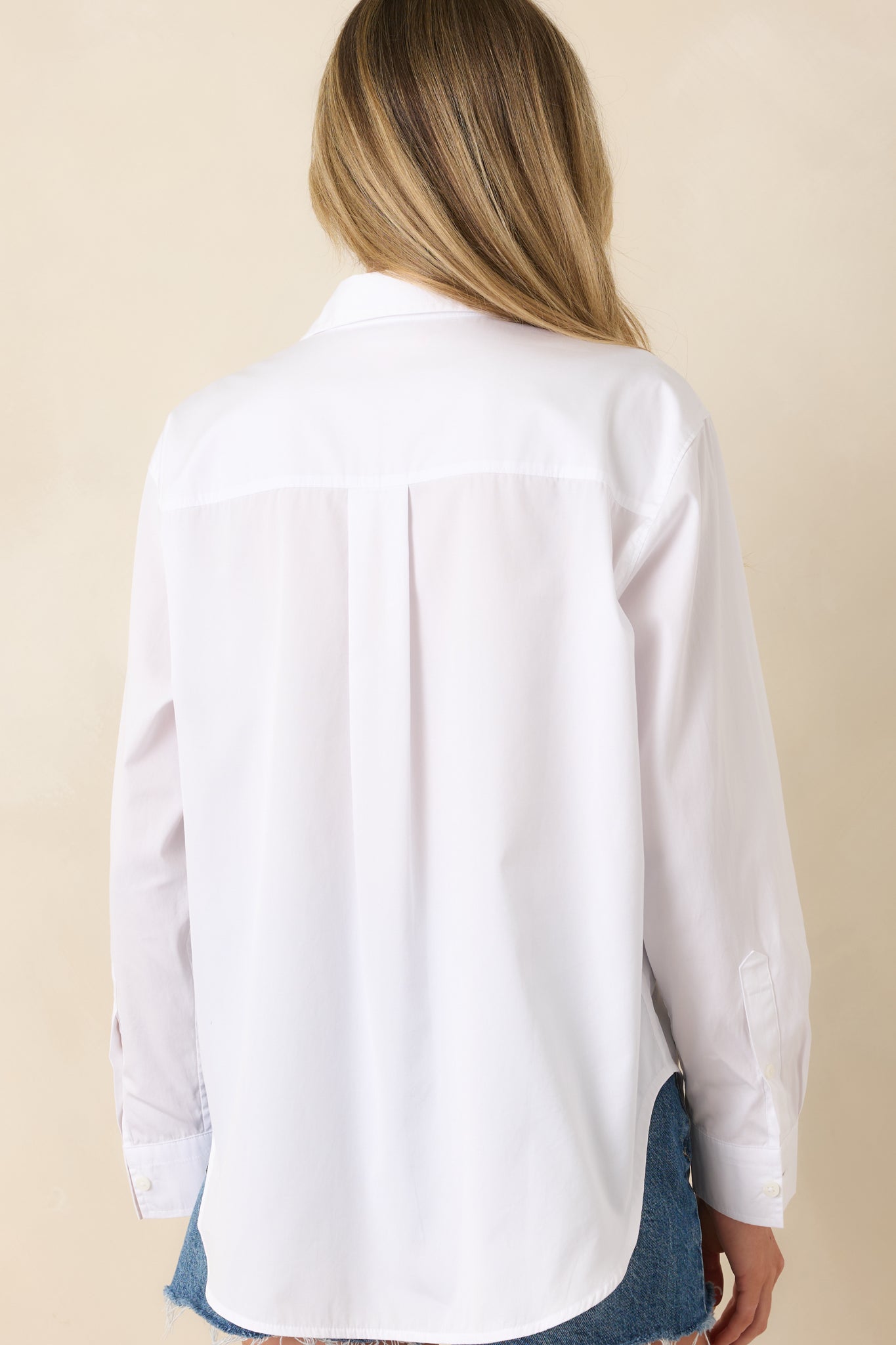 Rear view of white oversized button-up shirt with curved hemline and clean structured finish.