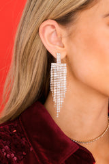 Styled shot of model wearing earrings that feature rhinestones with gold hardware backing, a dangle design, and a secure post backing.
