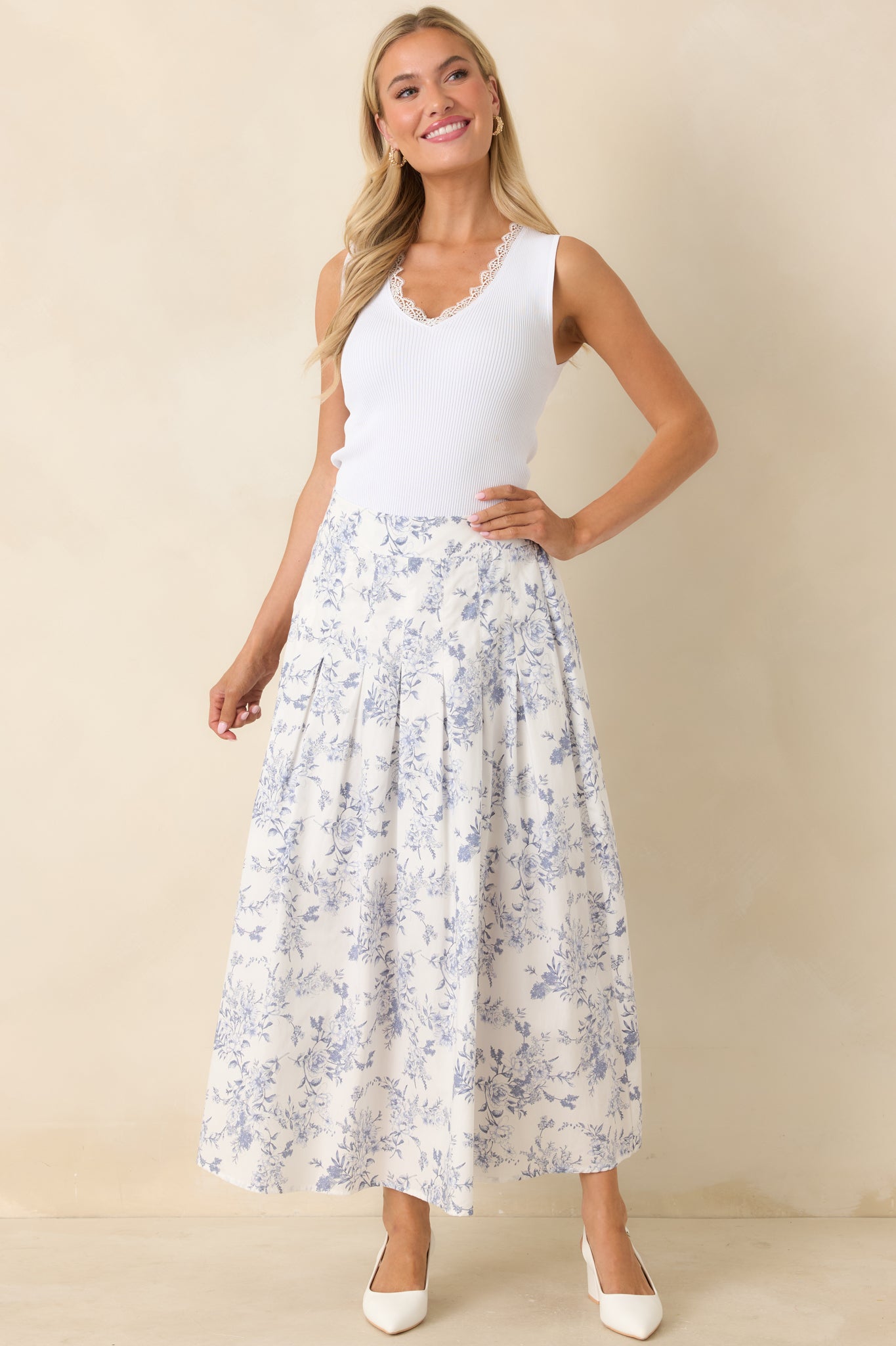 Woman wearing a white top and floral skirt against a beige background