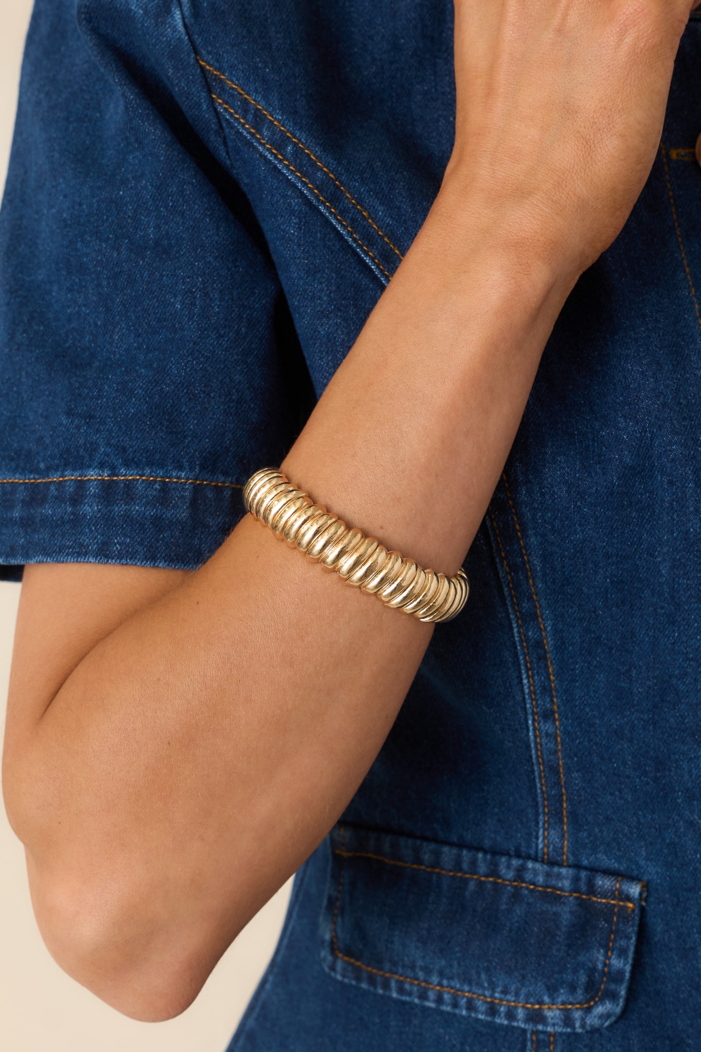 Close-up detail of gold bracelet showing ribbed texture, stretch band, and polished finish.