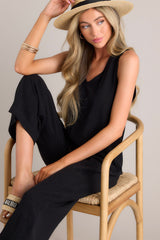 Seated close up view of this black jumpsuit that features a v-neckline, a lightweight material, a wide leg, and a slightly cropped hemline.