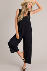 Angled full body view of this black jumpsuit that features a v-neckline, a lightweight material, a wide leg, and a slightly cropped hemline.