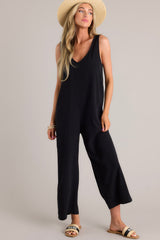 Full body view of this black jumpsuit that features a v-neckline, a lightweight material, a wide leg, and a slightly cropped hemline.