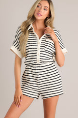 Angled front view of this stripe romper that features a collared neckline, a functional button front, a breast pocket, wide short sleeves, an elastic waistband, functional hip pockets, and a textured material.