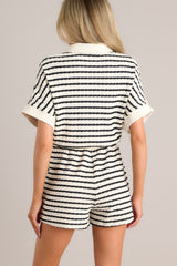 Back view of this stripe romper that features a collared neckline, a functional button front, a breast pocket, wide short sleeves, an elastic waistband, functional hip pockets, and a textured material.
