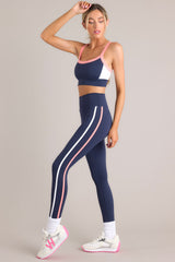 Full body side view of these leggings that feature a high waisted design, thick waistband, a pocket in the back of the waistband, and colored stripes down the legs.