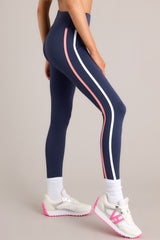 Close up side view of these leggings that feature a high waisted design, thick waistband, a pocket in the back of the waistband, and colored stripes down the legs.