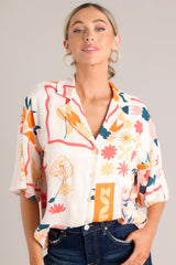 Close up front view of this apricot multi print top that features functional buttons down the front, a citrus and floral print design, a collared neckline, and lightweight fabric.