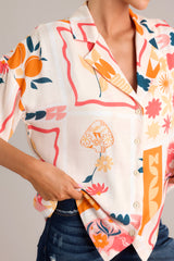 Close up view of the floral and citrus pattern, front buttons, and collared neckline on this apricot multi, short sleeve top. 