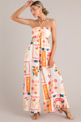 Head on view of a patterned jumpsuit featuring a halter tassel tie neckline, an elastic waist, cutouts at the waist, functional pockets, and a smocked insert in the back of the bust.