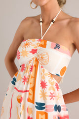 Zoom up view of a patterned jumpsuit featuring a halter tassel tie neckline, an elastic waist, cutouts at the waist, functional pockets, and a smocked insert in the back of the bust.