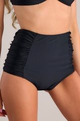 These black bikini bottoms feature a high waisted design, ruching on the sides, and a full coverage backside.