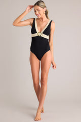 A full body view of this black one piece that features a v-neckline, a gold accent ring, shimmer detailing, a textured material, an open back, and a full coverage backside.