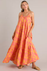 This pink and orange dress features a round neckline, non-adjustable braided straps, functional side pockets, and a wide, flowy fit. 