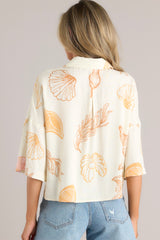 Back view of this ivory top featuring a collared neckline, a seashell print on lightweight fabric, and a slightly cropped length.