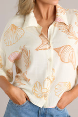 Close up view of this ivory top featuring a collared neckline, a seashell print on lightweight fabric, and a slightly cropped length.