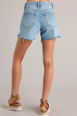 Back view of these medium wash denim shorts that feature a high-waist, a classic button-zipper closure, functional belt loops, functional front and back pockets, a small side slit at the bottom hem, and a raw hem.