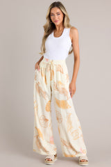 Full body straight view of these ivory pants featuring an elastic waistband, a drawstring tie, a wide leg design, and a beachy seashell print throughout.