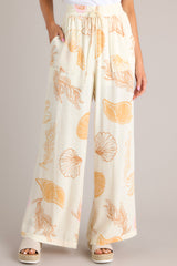 Front view of these ivory pants featuring an elastic waistband, a drawstring tie, a wide leg design, and a beachy seashell print throughout.