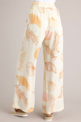 Back view of these ivory pants featuring an elastic waistband, a drawstring tie, a wide leg design, and a beachy seashell print throughout.
