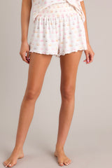Front view of these white shorts featuring a smocked elastic waistband, lettuce hemline, and lightweight sun print.