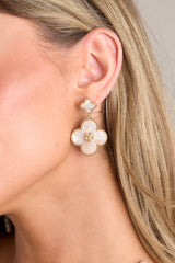 These white and gold earrings feature gold hardware, a clover shaped stud, a larger clover dangle with gold detailing, and secure post backings.