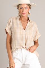 This beige top features a collared v-neckline, a lightweight material, functional buttons down the back, and cuffed short sleeves.