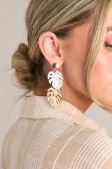 These white and gold earrings feature gold hardware, a marbled ivory color, monstera leaf drop detailing, and secure post backings.