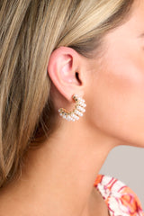 These gold and pearl earrings feature gold hardware, rows of faux pearls, an open circle design, and secure post backings.