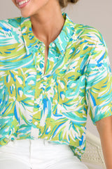 Close up view of this top that features a collared neckline, a full button front, a functional breast pocket, a vibrant print, and a split high-low hemline.