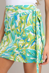 Close up view of this skirt that features a high waisted design, a discrete side zipper, a self-tie wrap feature, and a vibrant print.