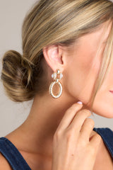 These gold earrings feature gold hardware, rhinestone detailing on stud, a textured dangle, and secure post backings.