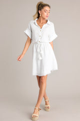 Full view of this dress that features a collared neckline, a partial button front, a self-tie drawstring waist, a raw hemline, and thick cuffed sleeves.