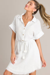 Front view of this dress that features a collared neckline, a partial button front, a self-tie drawstring waist, a raw hemline, and thick cuffed sleeves.