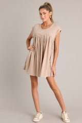 Angled full body  view of this tan mini dress that features a crew neckline, contrasting materials, functional pockets, and folded cuffed sleeves.