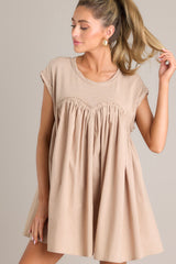 This tan mini dress features a crew neckline, contrasting materials, functional pockets, and folded cuffed sleeves.