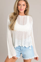 Front view of this top that features a high rounded neckline, a soft material, an open-knit crochet design, scalloped long sleeves, and a scalloped hemline.